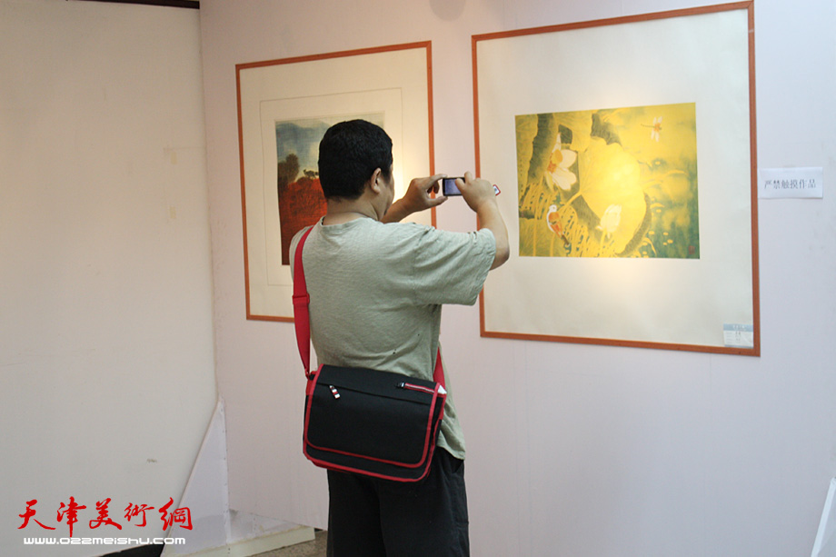 来宾参观画作，并用手机拍照。 