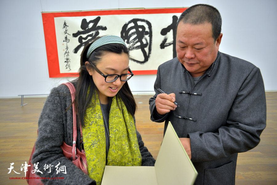 中国梦·天容海色——马孟杰书法作品展在天津美术馆举办。图为马孟杰为观众在其书法集上签名留念。