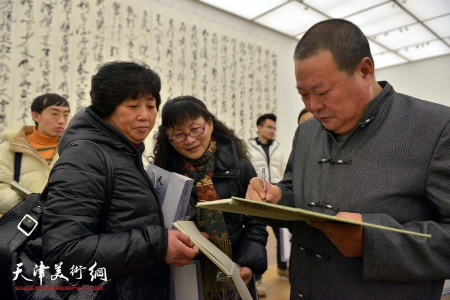 中国梦·天容海色——马孟杰书法作品展在天津美术馆举办。图为马孟杰为观众在其书法集上签名留念。