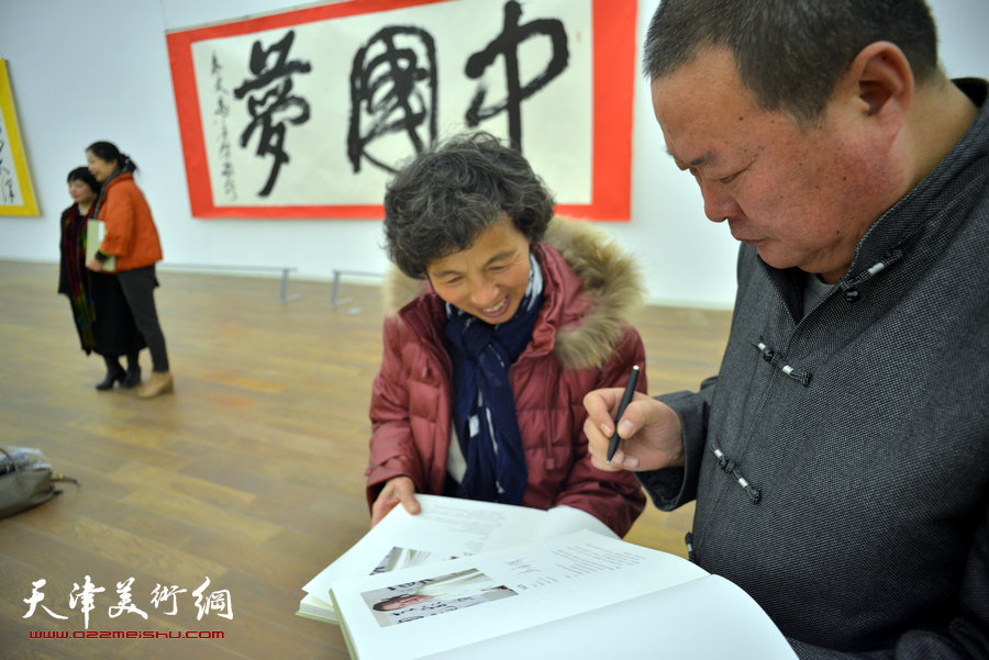 中国梦·天容海色——马孟杰书法作品展在天津美术馆举办。图为马孟杰为观众在其书法集上签名留念。